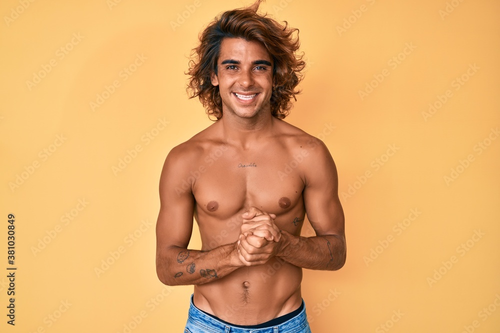 Young hispanic man standing shirtless with hands together and crossed fingers smiling relaxed and cheerful. success and optimistic