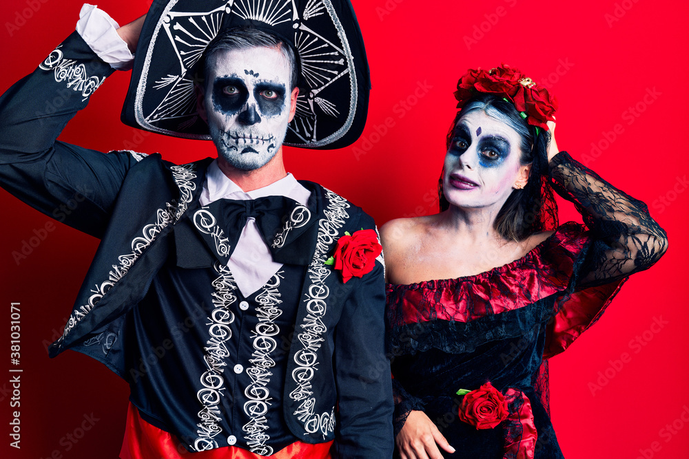 Young couple wearing mexican day of the dead costume over red confuse and wonder about question. uncertain with doubt, thinking with hand on head. pensive concept. Young couple wearing mexican day of the dead costume over red confuse and wonder about question. uncertain with doubt, thinking with hand on head. pensive concept.