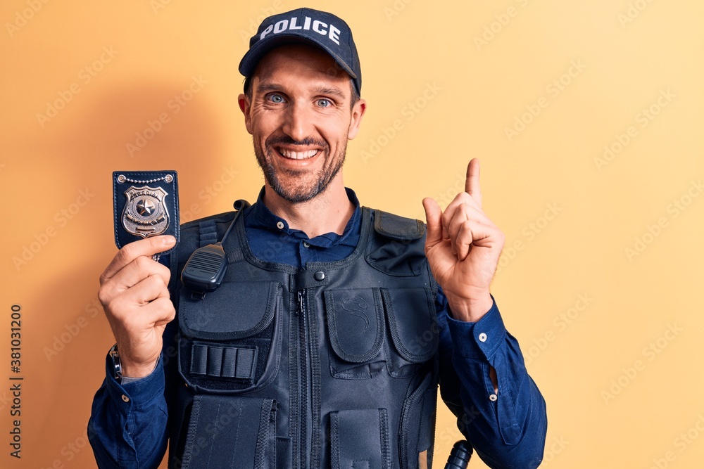 Young handsome policeman wearing uniform and bulletprof holding police badge smiling happy pointing with hand and finger to the side Young handsome policeman wearing uniform and bulletprof holding police badge smiling happy pointing with hand and finger to the side