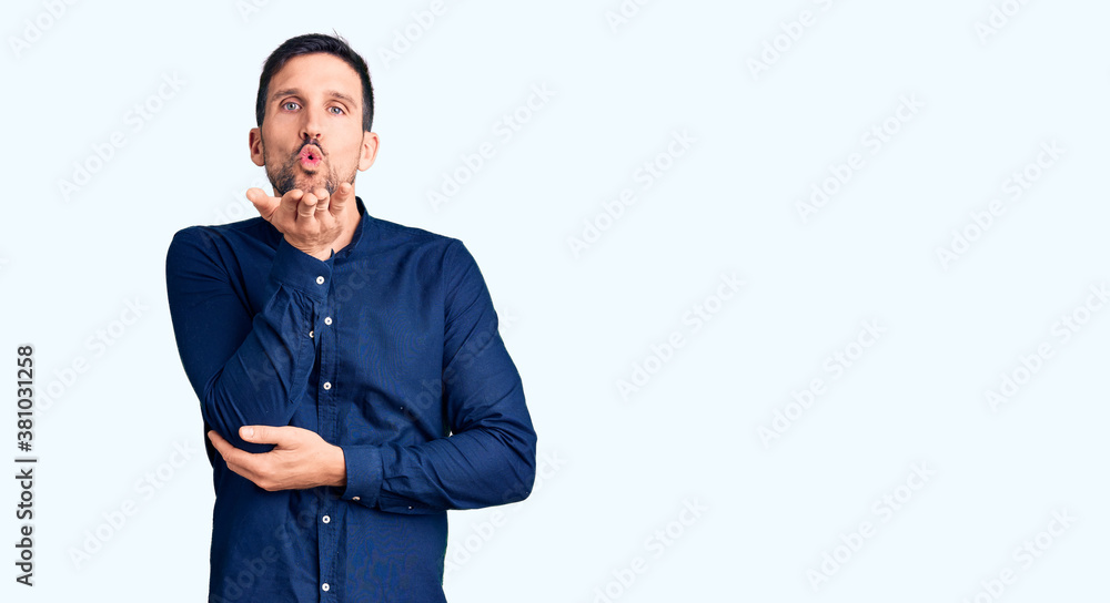 Young handsome man wearing casual shirt looking at the camera blowing a kiss with hand on air being lovely and sexy. love expression. Young handsome man wearing casual shirt looking at the camera blowing a kiss with hand on air being lovely and sexy. love expression.