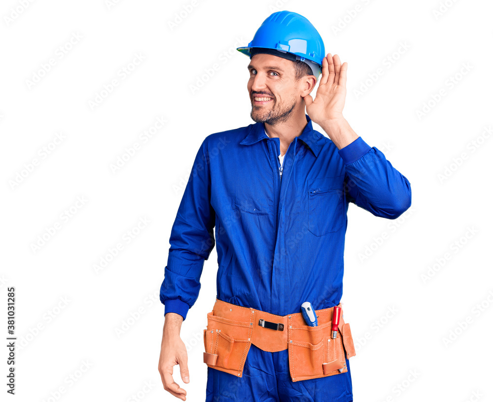Young handsome man wearing worker uniform and hardhat smiling with hand over ear listening an hearing to rumor or gossip. deafness concept. Young handsome man wearing worker uniform and hardhat smiling with hand over ear listening an hearing to rumor or gossip. deafness concept.