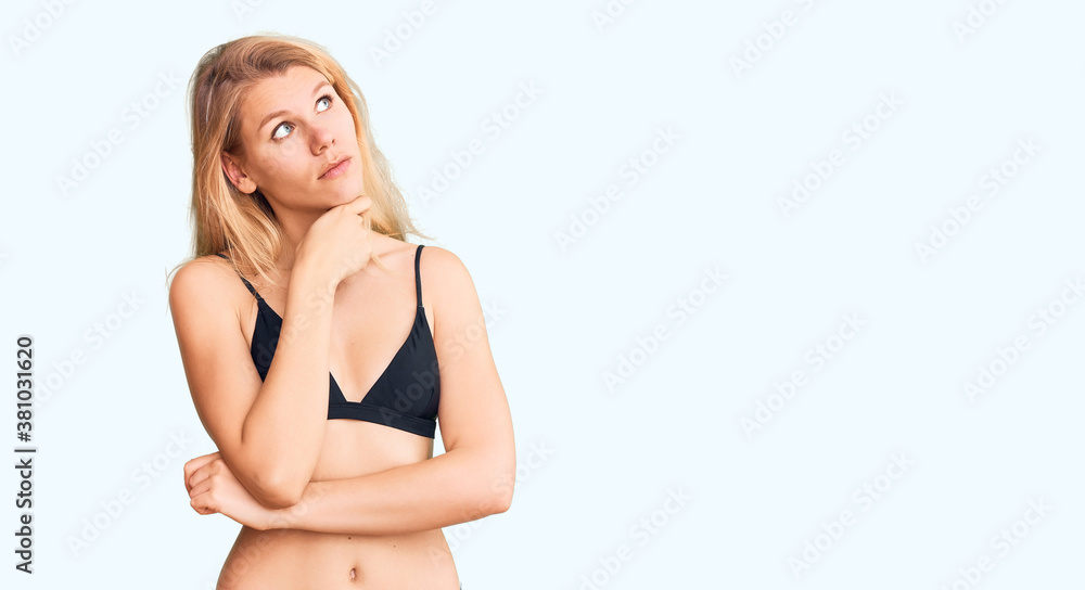 Fototapeta premium Young beautiful blonde woman wearing bikini with hand on chin thinking about question, pensive expression. smiling with thoughtful face. doubt concept.