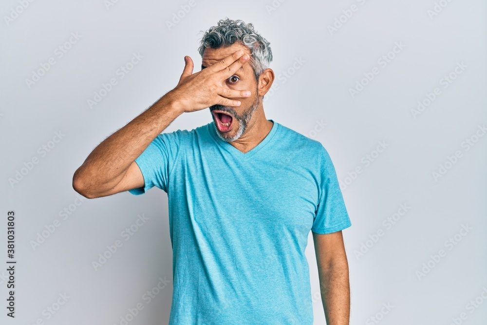 Middle age grey-haired man wearing casual clothes peeking in shock covering face and eyes with hand, looking through fingers with embarrassed expression. Middle age grey-haired man wearing casual clothes peeking in shock covering face and eyes with hand, looking through fingers with embarrassed expression.