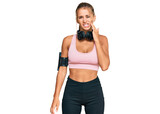 Young blonde woman wearing gym clothes and using headphones touching mouth with hand with painful expression because of toothache or dental illness on teeth. dentist