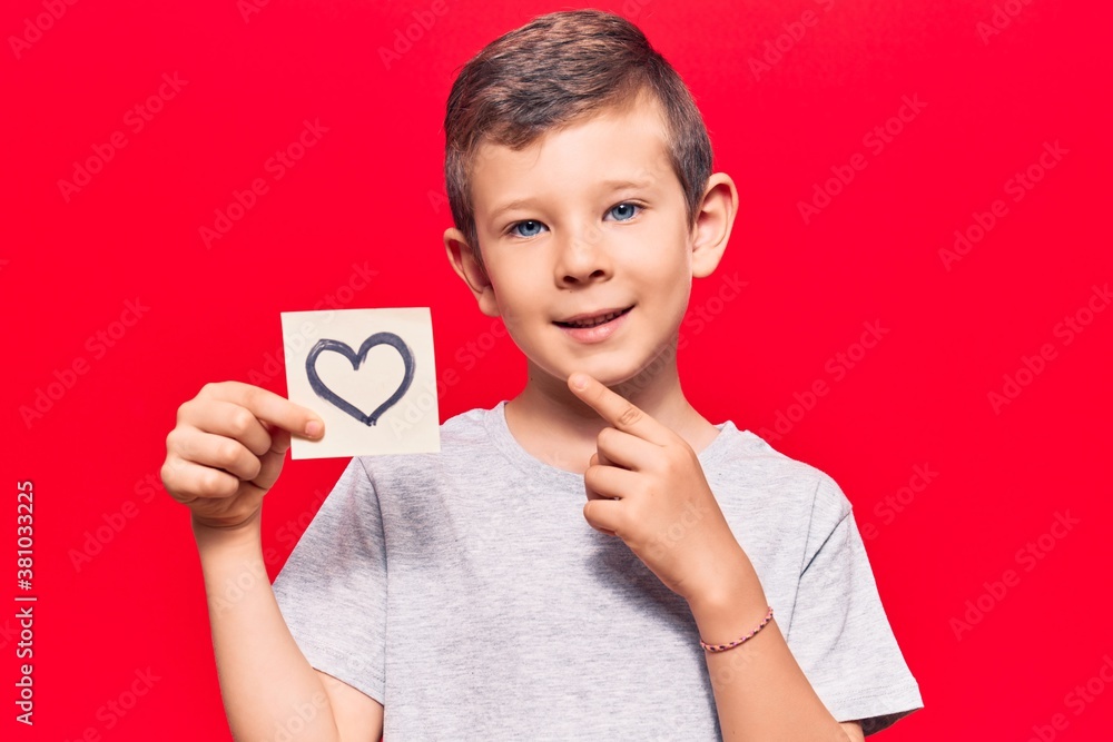 Cute blond kid holding heart reminder smiling happy pointing with hand and finger Cute blond kid holding heart reminder smiling happy pointing with hand and finger