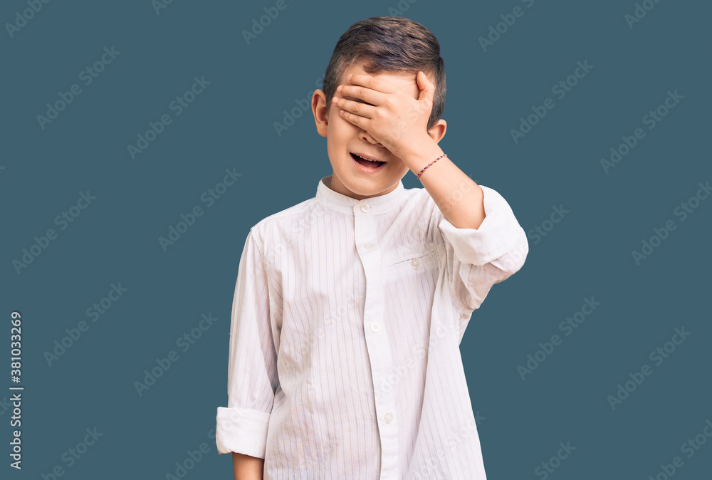 Cute blond kid wearing elegant shirt smiling and laughing with hand on face covering eyes for surprise. blind concept. Cute blond kid wearing elegant shirt smiling and laughing with hand on face covering eyes for surprise. blind concept.