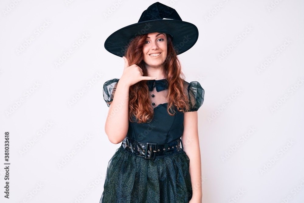 Young beautiful woman wearing witch halloween costume smiling doing phone gesture with hand and fingers like talking on the telephone. communicating concepts. Young beautiful woman wearing witch halloween costume smiling doing phone gesture with hand and fingers like talking on the telephone. communicating concepts.