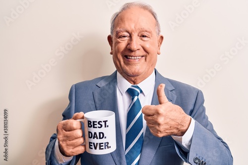 Handsome grey-haired man wearing suit drinking cup of coffee with best dad ever message smiling happy and positive, thumb up doing excellent and approval sign © Krakenimages.com