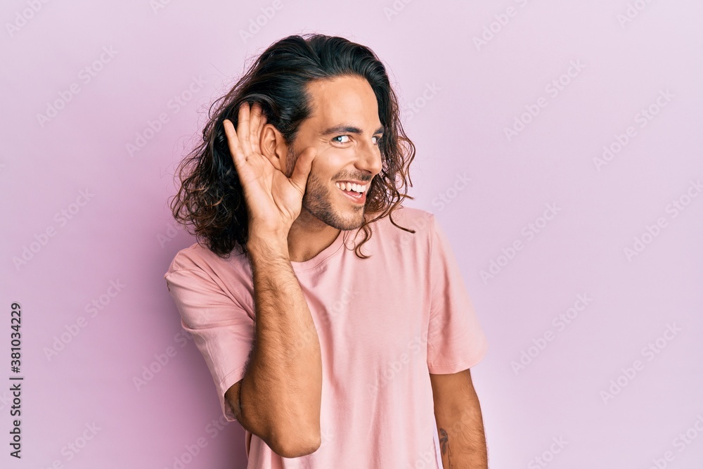 Young handsome man with long hair wearing casual clothes smiling with hand over ear listening and hearing to rumor or gossip. deafness concept. Young handsome man with long hair wearing casual clothes smiling with hand over ear listening and hearing to rumor or gossip. deafness concept.