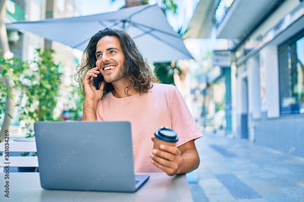 Young hispanic man smiling happy working using laptop and talking on thesmartphone at terrace of coffee shop. Young hispanic man smiling happy working using laptop and talking on thesmartphone at terrace of coffee shop.