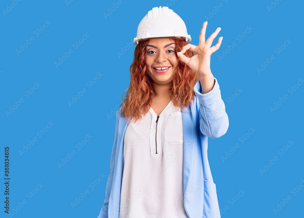 Young latin woman wearing architect hardhat smiling positive doing ok sign with hand and fingers. successful expression. Young latin woman wearing architect hardhat smiling positive doing ok sign with hand and fingers. successful expression.