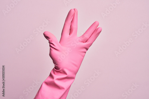 Hand of caucasian young man with cleaning glove over isolated pink background greeting doing Vulcan salute, showing hand palm and fingers, freak culture