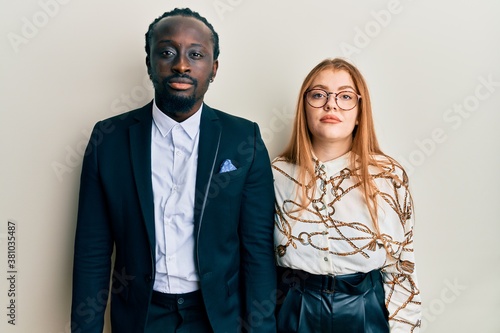 Young interracial couple wearing business and elegant clothes relaxed with serious expression on face. simple and natural looking at the camera.