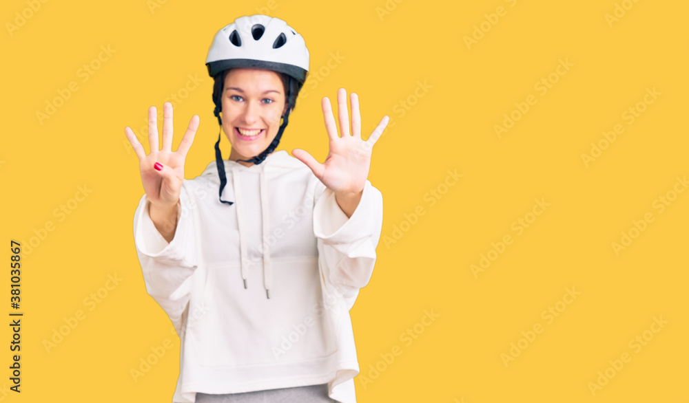 Beautiful brunette young woman wearing bike helmet and sporty clothes showing and pointing up with fingers number nine while smiling confident and happy. Beautiful brunette young woman wearing bike helmet and sporty clothes showing and pointing up with fingers number nine while smiling confident and happy.