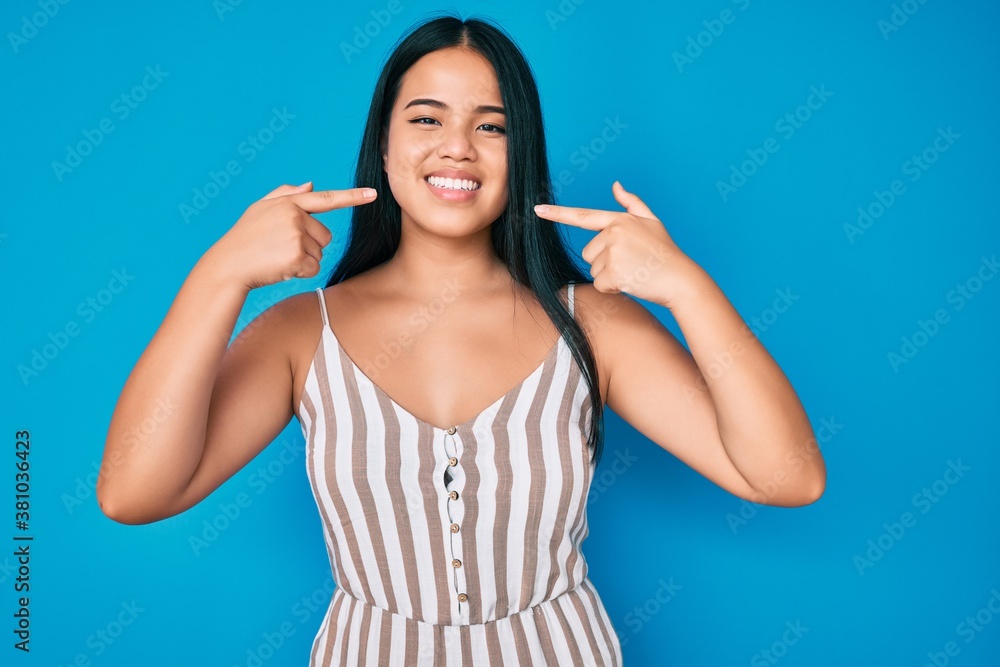 Fototapeta premium Young beautiful asian girl wearing casual clothes smiling cheerful showing and pointing with fingers teeth and mouth. dental health concept.