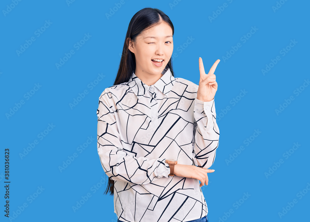 Young beautiful chinese woman wearing casual shirt smiling with happy face winking at the camera doing victory sign with fingers. number two. Young beautiful chinese woman wearing casual shirt smiling with happy face winking at the camera doing victory sign with fingers. number two.