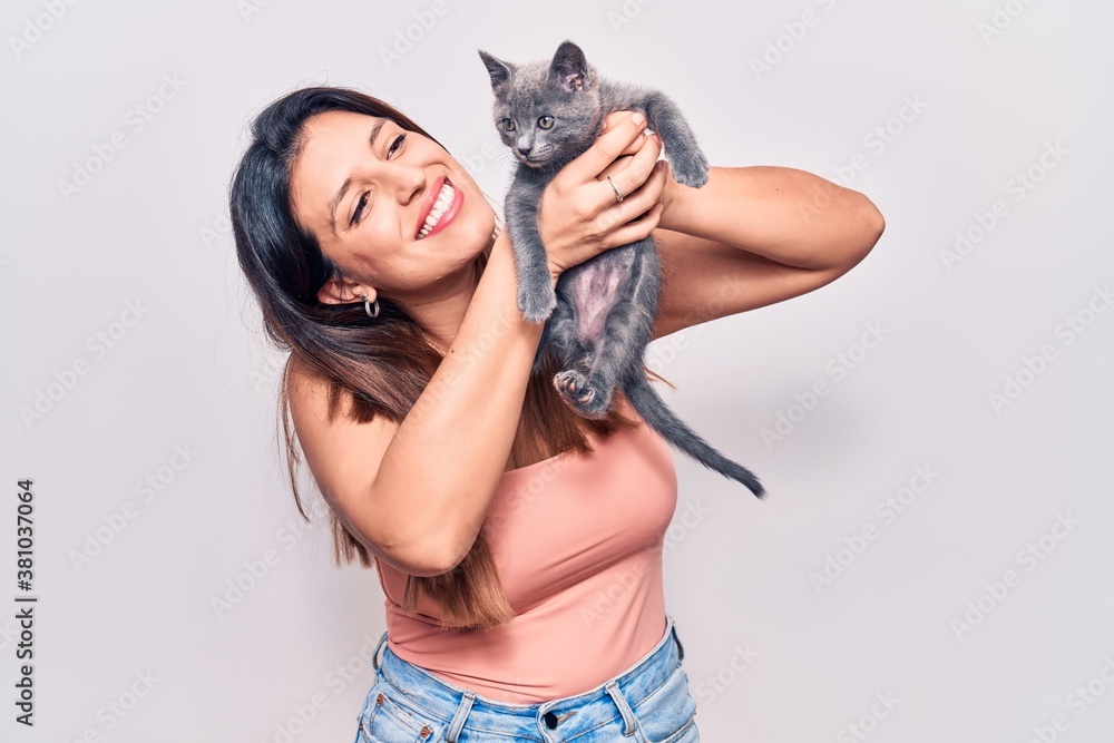 Young beautiful latin woman smilling happy. Standing with smile on face holding adorable cat over isolated white backgroun Young beautiful latin woman smilling happy. Standing with smile on face holding adorable cat over isolated white backgroun