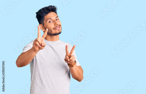 Handsome latin american young man wearing casual tshirt smiling looking to the camera showing fingers doing victory sign. number two. photo