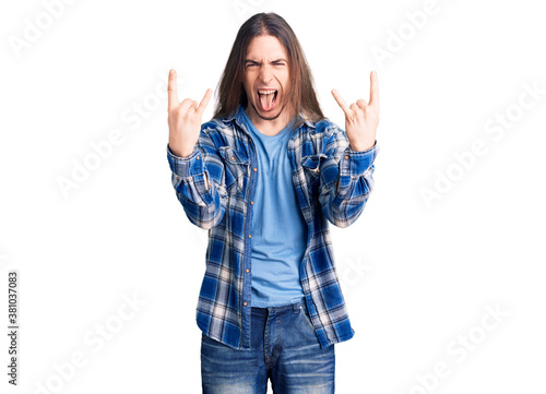 Young adult man with long hair wearing casual shirt shouting with crazy expression doing rock symbol with hands up. music star. heavy concept.
