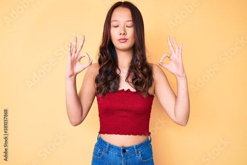 Young beautiful chinese girl wearing summer clothes relax and smiling with eyes closed doing meditation gesture with fingers. yoga concept.