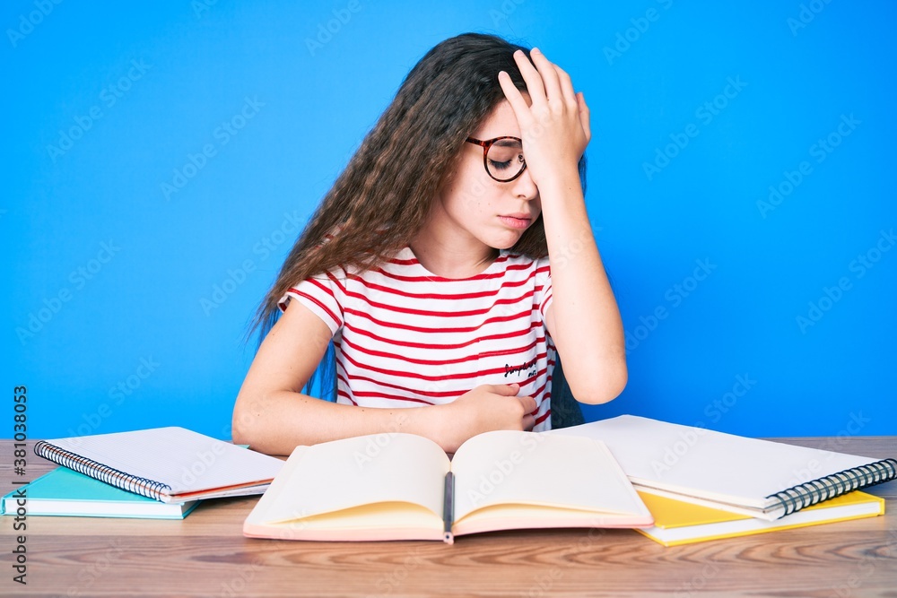 Cute hispanic child girl studying for school exam sitting on the table surprised with hand on head for mistake, remember error. forgot, bad memory concept. Cute hispanic child girl studying for school exam sitting on the table surprised with hand on head for mistake, remember error. forgot, bad memory concept.