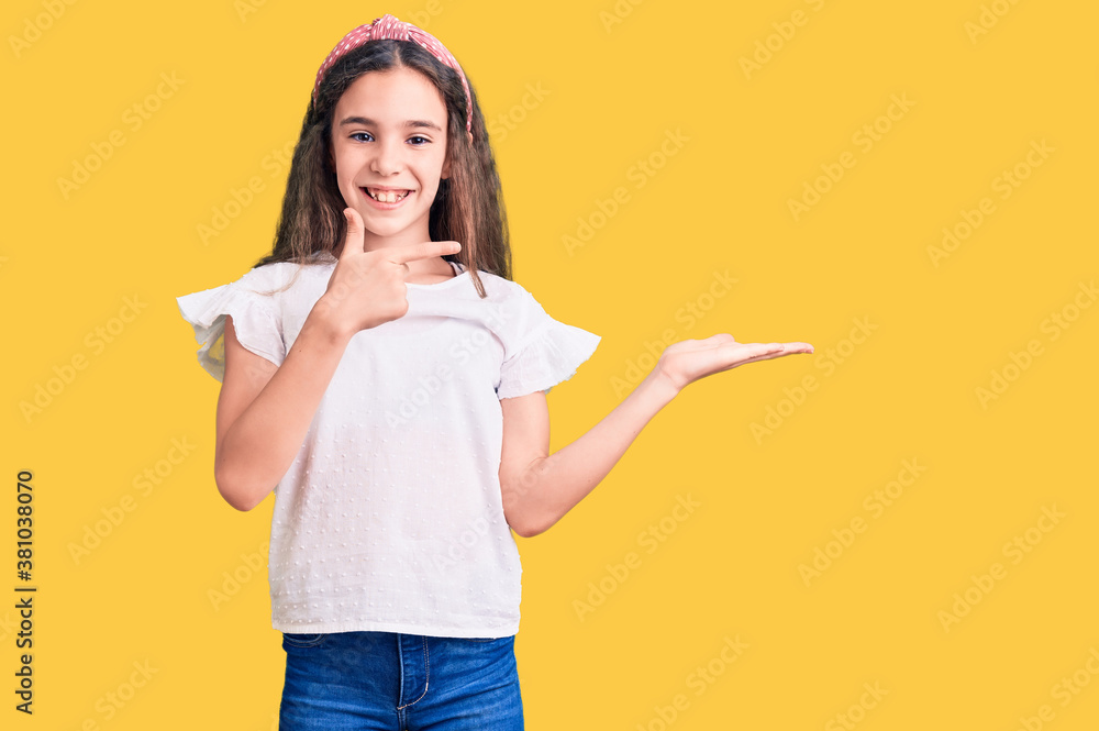 Cute hispanic child girl wearing casual white tshirt amazed and smiling to the camera while presenting with hand and pointing with finger. Cute hispanic child girl wearing casual white tshirt amazed and smiling to the camera while presenting with hand and pointing with finger.
