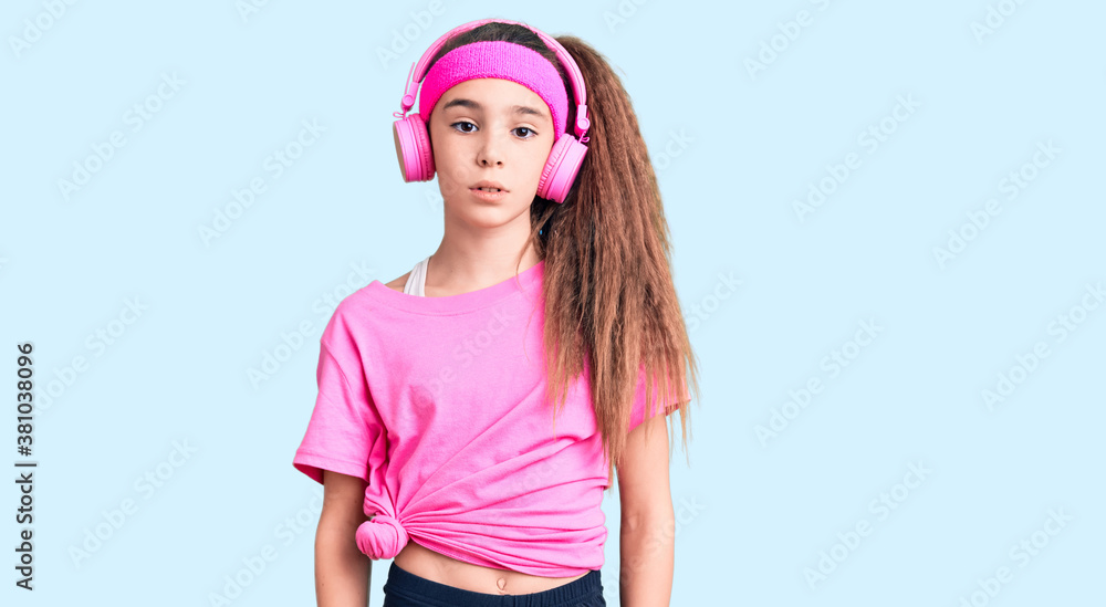Cute hispanic child girl wearing gym clothes and using headphones relaxed with serious expression on face. simple and natural looking at the camera. Cute hispanic child girl wearing gym clothes and using headphones relaxed with serious expression on face. simple and natural looking at the camera.