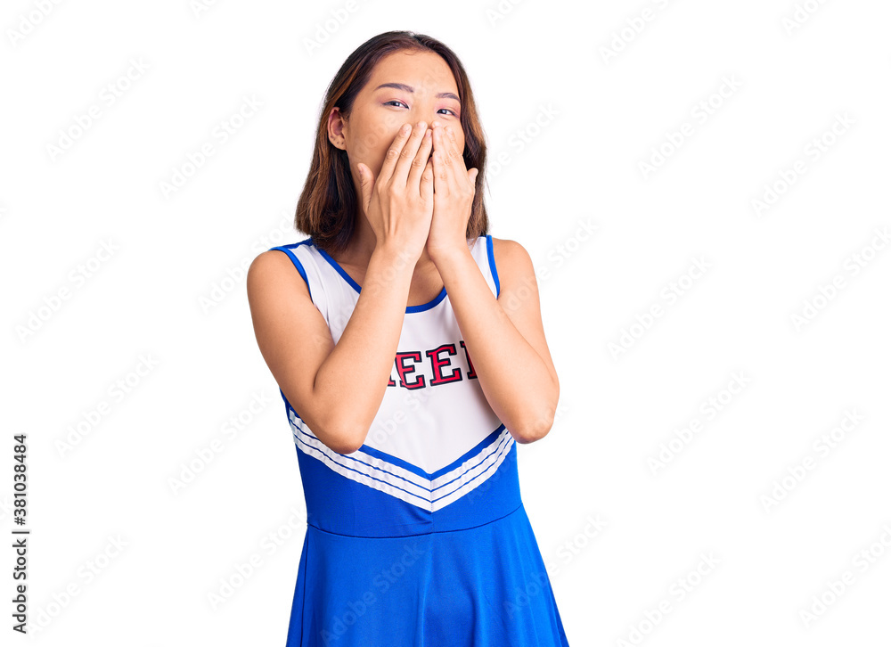 Young beautiful chinese girl wearing cheerleader uniform laughing and embarrassed giggle covering mouth with hands, gossip and scandal concept Young beautiful chinese girl wearing cheerleader uniform laughing and embarrassed giggle covering mouth with hands, gossip and scandal concept