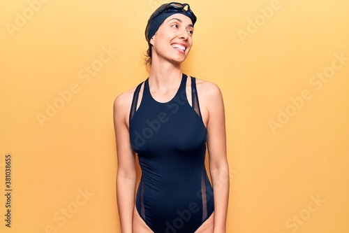 Young beautiful hispanic woman wearing swimwear and swimmer glasses looking away to side with smile on face, natural expression. laughing confident.
