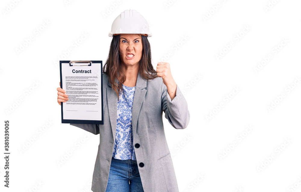 Young beautiful brunette woman wearing architect hardhat holding contract annoyed and frustrated shouting with anger, yelling crazy with anger and hand raised