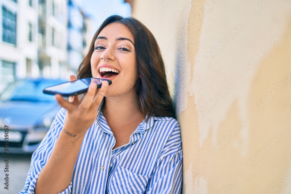 Fototapeta premium Young hispanic businesswoman smiling happy sending voice message using smartphone at the city.