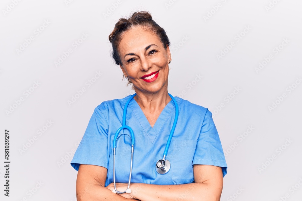 Middle age brunette nurse woman wearing uniform and stethoscope over white background happy face smiling with crossed arms looking at the camera. Positive person. - obrazy, fototapety, plakaty 