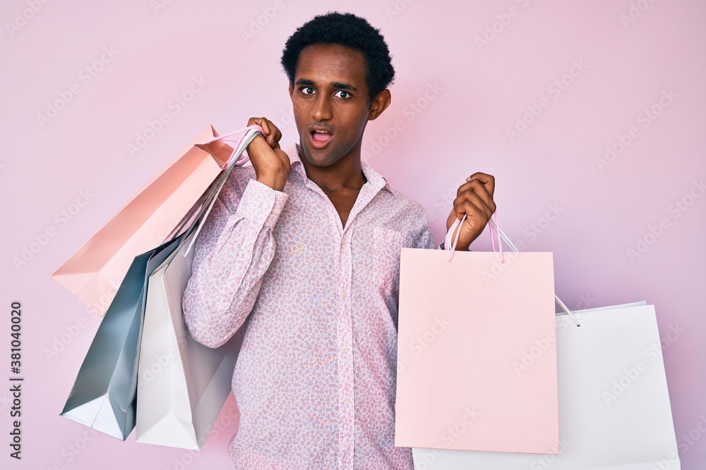 African handsome man holding shopping bags in shock face, looking skeptical and sarcastic, surprised with open mouth African handsome man holding shopping bags in shock face, looking skeptical and sarcastic, surprised with open mouth