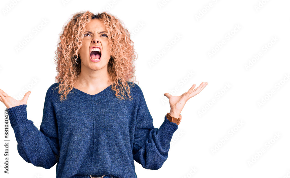 Young blonde woman with curly hair wearing casual winter sweater crazy and mad shouting and yelling with aggressive expression and arms raised. frustration concept. Young blonde woman with curly hair wearing casual winter sweater crazy and mad shouting and yelling with aggressive expression and arms raised. frustration concept.