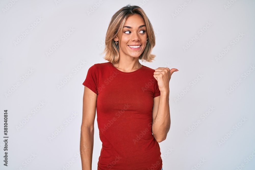 Beautiful caucasian woman wearing casual clothes smiling with happy face looking and pointing to the side with thumb up. Beautiful caucasian woman wearing casual clothes smiling with happy face looking and pointing to the side with thumb up.