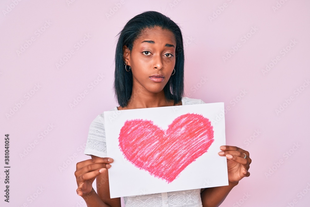 Young african american woman holding heart draw relaxed with serious expression on face. simple and natural looking at the camera. Young african american woman holding heart draw relaxed with serious expression on face. simple and natural looking at the camera.