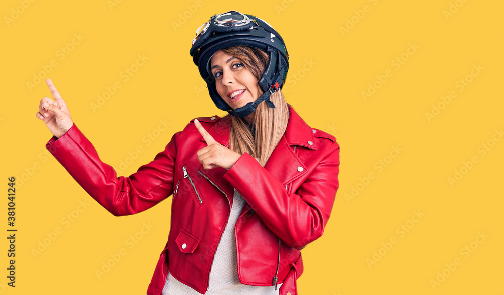 Young beautiful woman wearing motorcycle helmet smiling and looking at the camera pointing with two hands and fingers to the side. Young beautiful woman wearing motorcycle helmet smiling and looking at the camera pointing with two hands and fingers to the side.