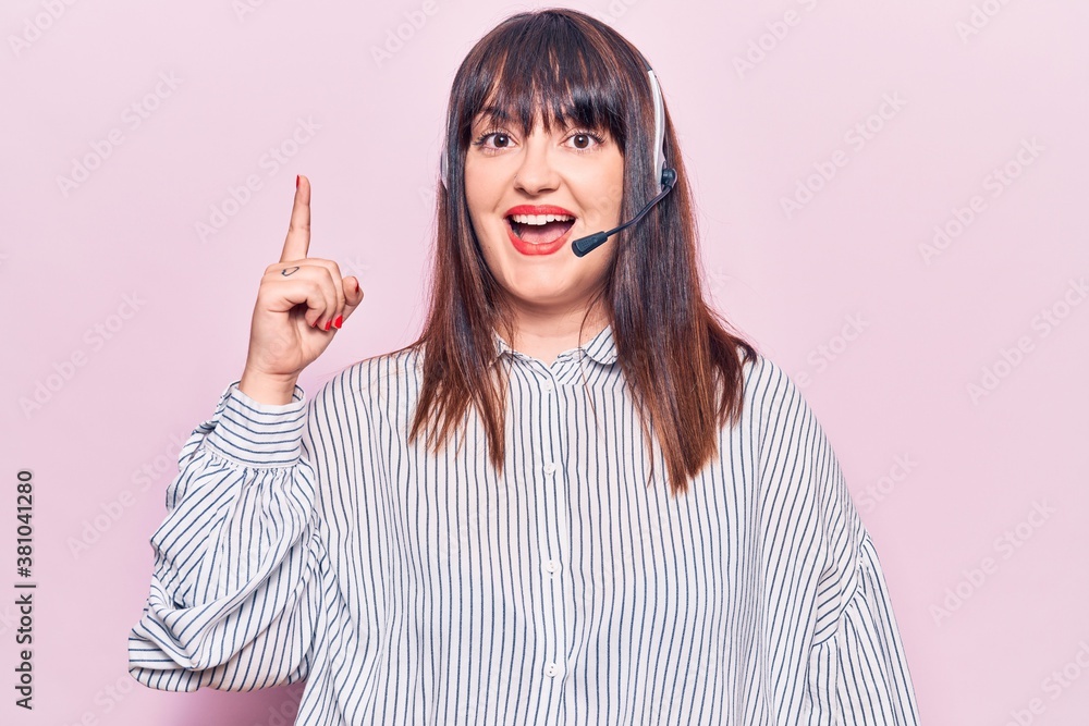 Young plus size woman wearing call center agent headset pointing finger up with successful idea. exited and happy. number one. Young plus size woman wearing call center agent headset pointing finger up with successful idea. exited and happy. number one.