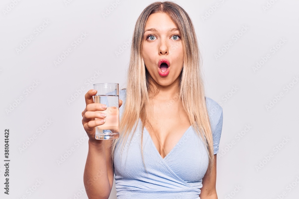 Young beautiful blonde girl drinking glass of water scared and amazed with open mouth for surprise, disbelief face Young beautiful blonde girl drinking glass of water scared and amazed with open mouth for surprise, disbelief face