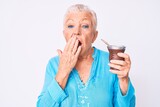 Senior beautiful woman with blue eyes and grey hair drinking mate infusion covering mouth with hand, shocked and afraid for mistake. surprised expression
