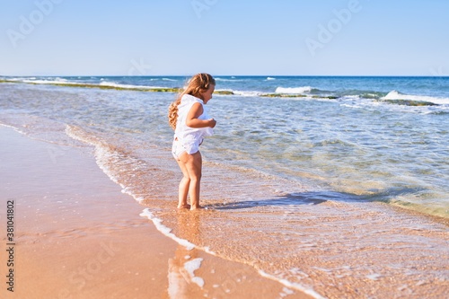Adorable blonde child on back view wearing summer dress playing on the sand at the beach © Krakenimages.com