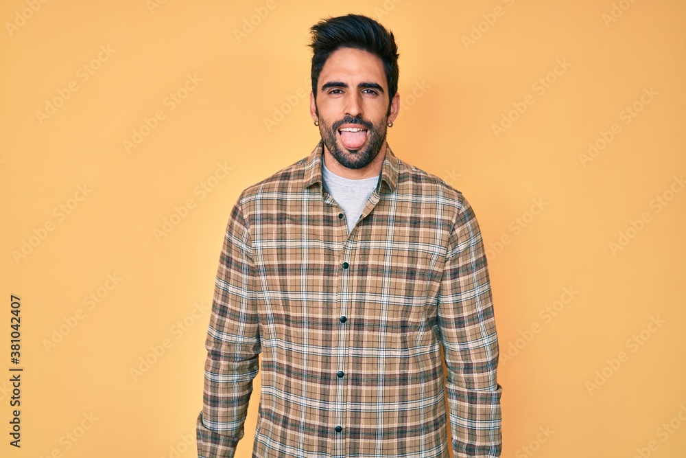 Handsome hispanic man with beard wearing casual clothes sticking tongue out happy with funny expression. emotion concept.