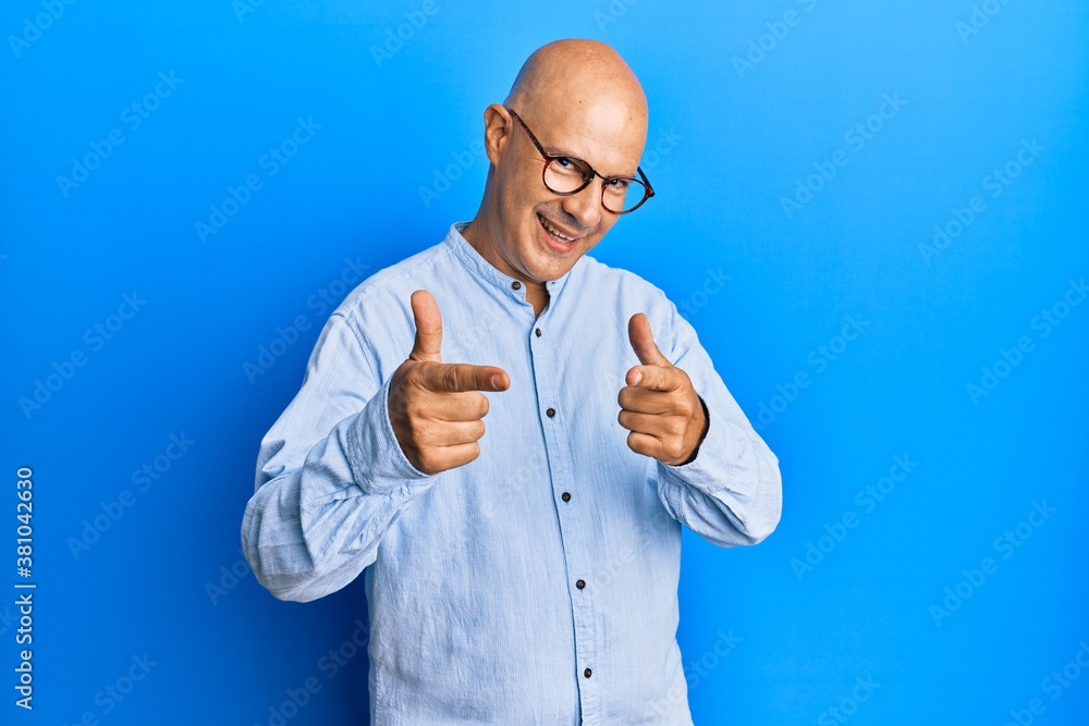 Middle age bald man wearing casual clothes and glasses pointing fingers to camera with happy and funny face. good energy and vibes. Middle age bald man wearing casual clothes and glasses pointing fingers to camera with happy and funny face. good energy and vibes.