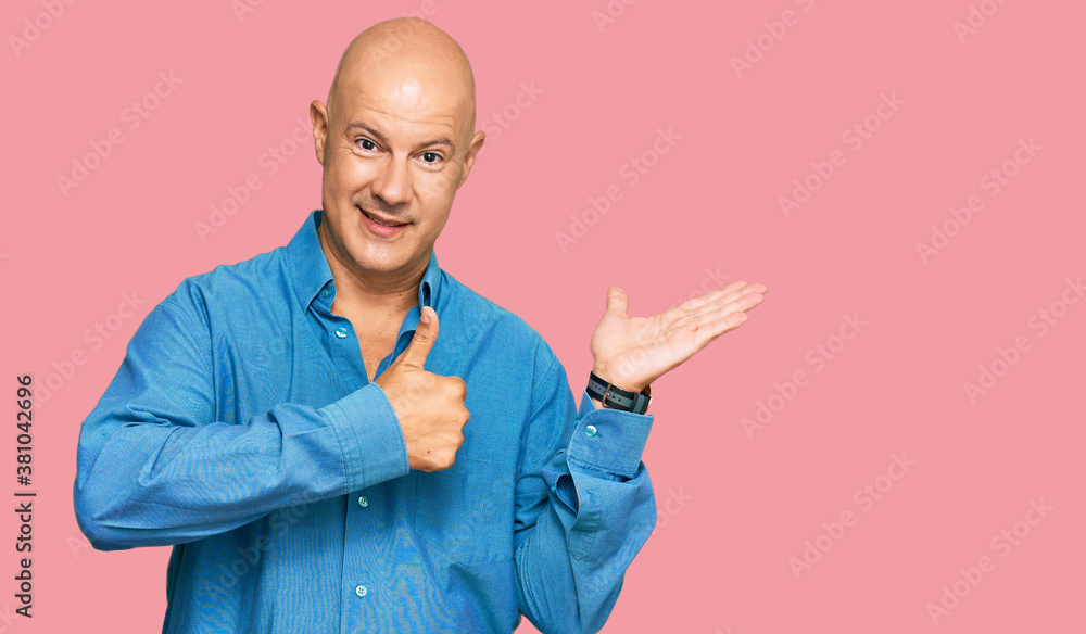 Middle age bald man wearing casual clothes showing palm hand and doing ok gesture with thumbs up, smiling happy and cheerful Middle age bald man wearing casual clothes showing palm hand and doing ok gesture with thumbs up, smiling happy and cheerful