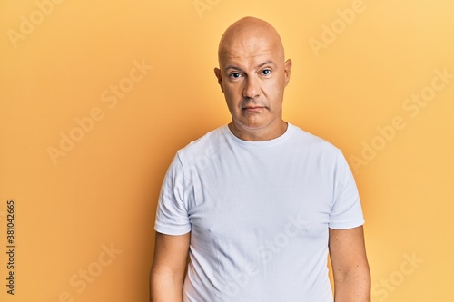 Middle age bald man wearing casual white tshirt with serious expression on face. simple and natural looking at the camera.