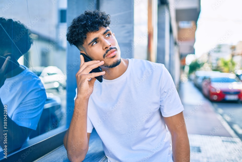 Young arab man with serious expression talking on the smartphone leaning on the wall. Young arab man with serious expression talking on the smartphone leaning on the wall.