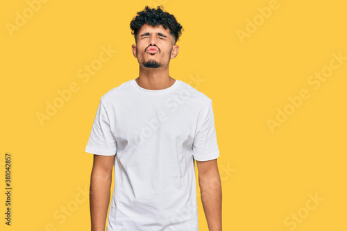 Young arab man wearing casual white t shirt looking at the camera blowing a kiss on air being lovely and sexy. love expression.
