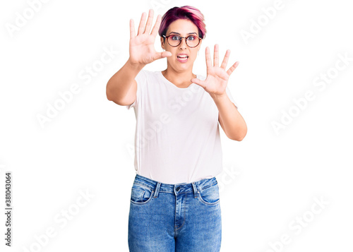 Young beautiful woman with pink hair wearing casual clothes and glasses afraid and terrified with fear expression stop gesture with hands, shouting in shock. panic concept.