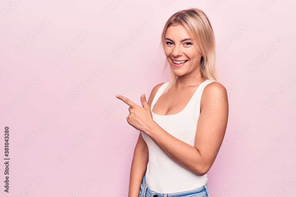 Young beautiful blonde woman wearing casual t-shirt standing over isolated pink background smiling cheerful pointing with hand and finger up to the side Young beautiful blonde woman wearing casual t-shirt standing over isolated pink background smiling cheerful pointing with hand and finger up to the side