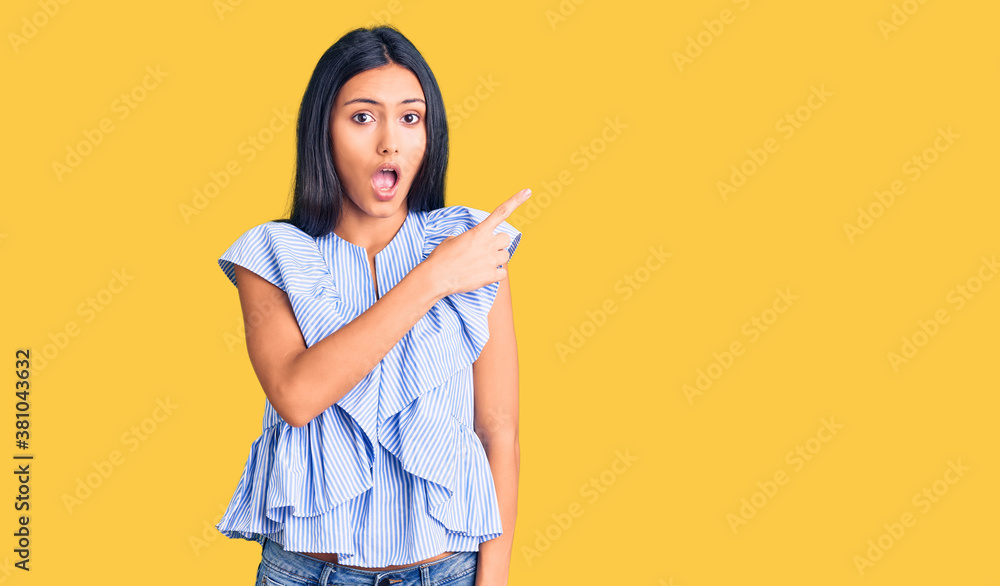 Young beautiful latin girl wearing casual clothes surprised pointing with finger to the side, open mouth amazed expression. Young beautiful latin girl wearing casual clothes surprised pointing with finger to the side, open mouth amazed expression.